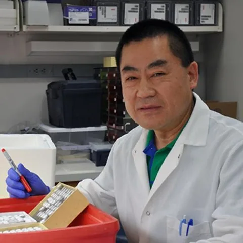 Portrait of Dr. Xin Chen in a white coat, working in the lab